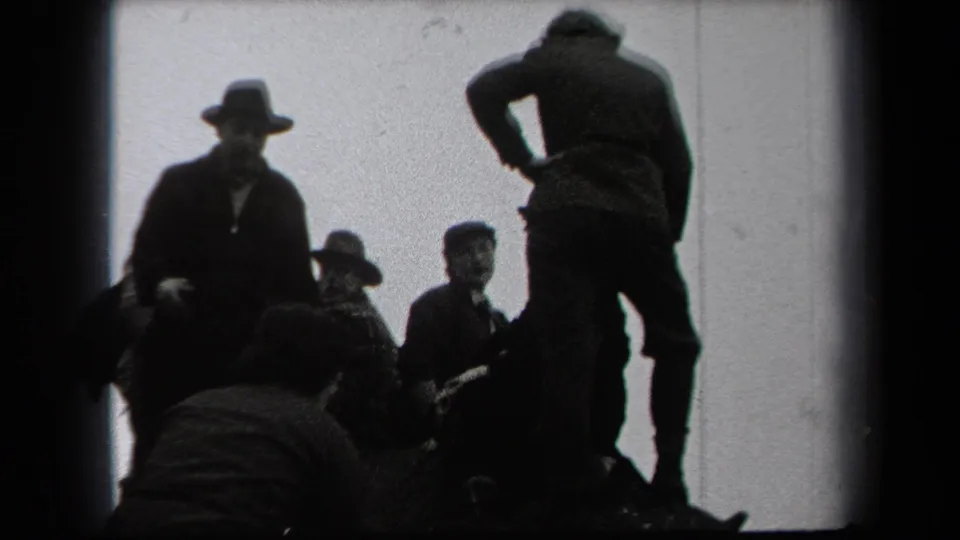 1938 New York home-movie frame showing adult men in dark coats and hats gathered outdoors near bare trees and brush.