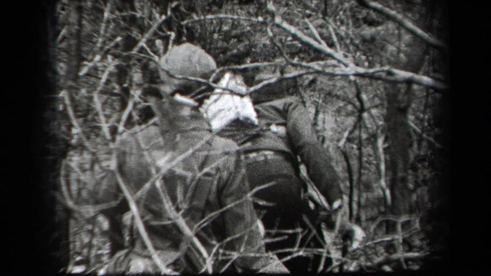 Adult men in coats and hats appear to push through tangled brush in a wooded New York setting, based on the supplied metadata.