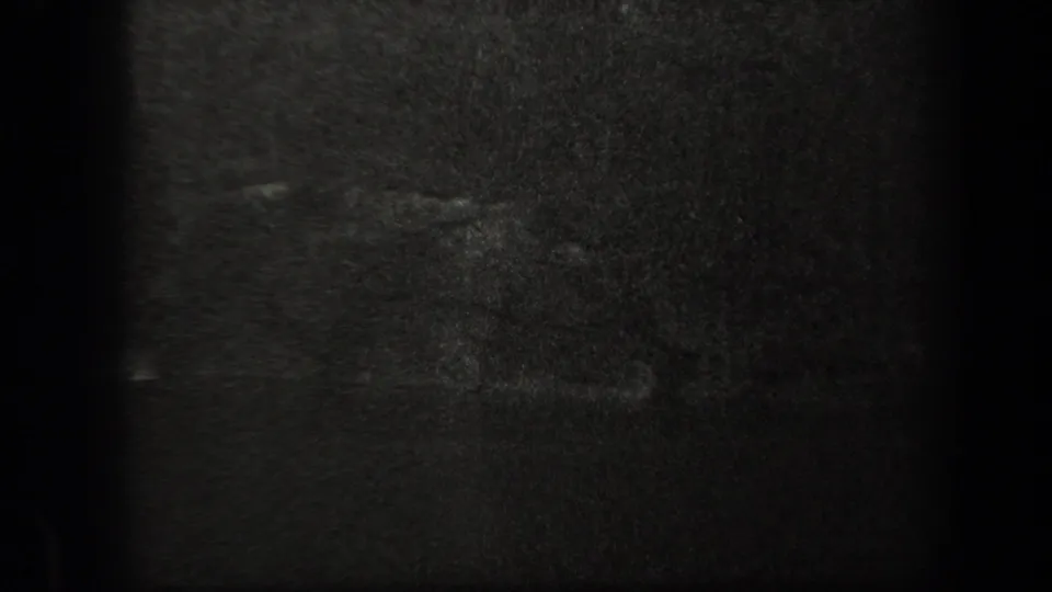 The image becomes very dark and indistinct, with grainy 8mm texture and only faint shapes suggesting ground or reel-end exposure change.