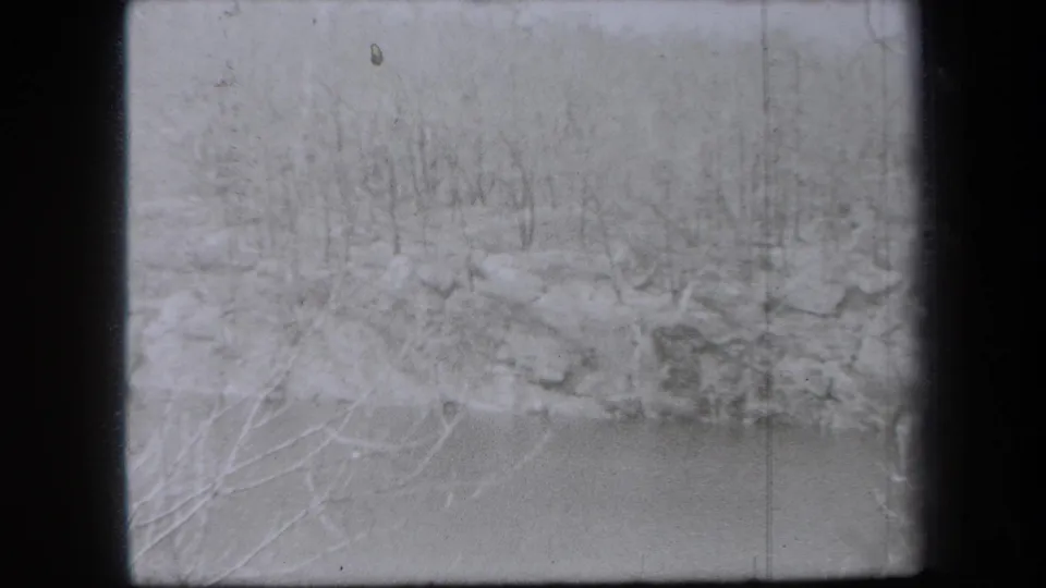1938 New York 8mm frame panning to a soft wide view of a rocky wooded bank above pale water or open ground.