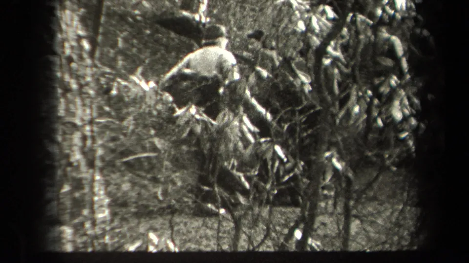 A man appears to climb or scramble through underbrush on a rocky forest slope in 1938 New York home-movie footage.