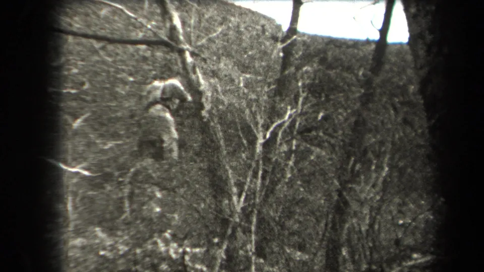 A man is seen at a distance on a wooded hillside with bare branches and uneven rocky ground, consistent with the supplied 1938 New York setting.
