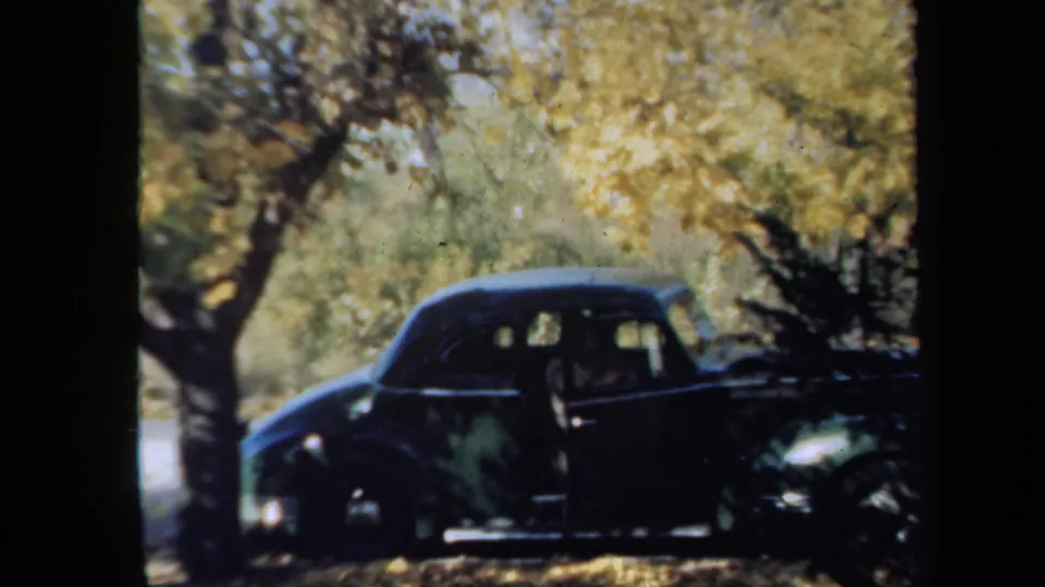1939 New York 8mm frame showing a dark rounded sedan under golden trees, with a person partly visible at the side door.