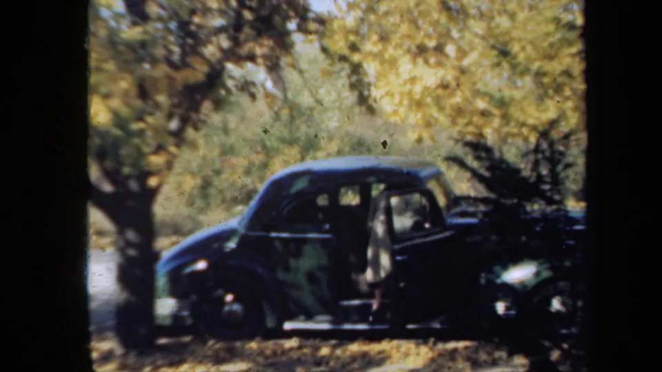 1939 New York home-movie frame of a person beside an open sedan door, with golden leaves and heavy 8mm borders visible.