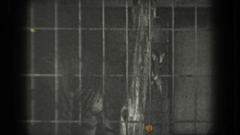 A tiger appears partly obscured behind square metal cage bars in dark black-and-white 8mm zoo footage.