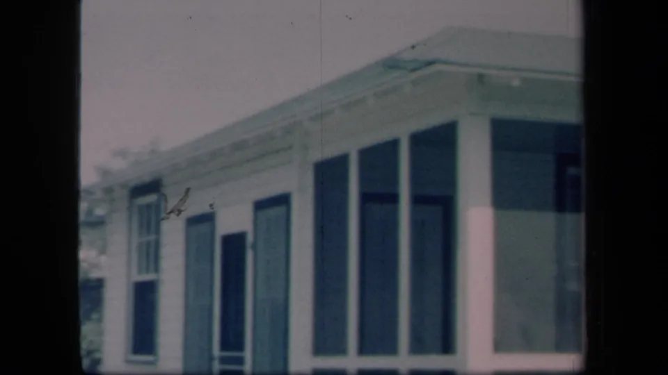 1958 New York home-movie view of a screened porch corner, tall windows and dark shutters on a white house.