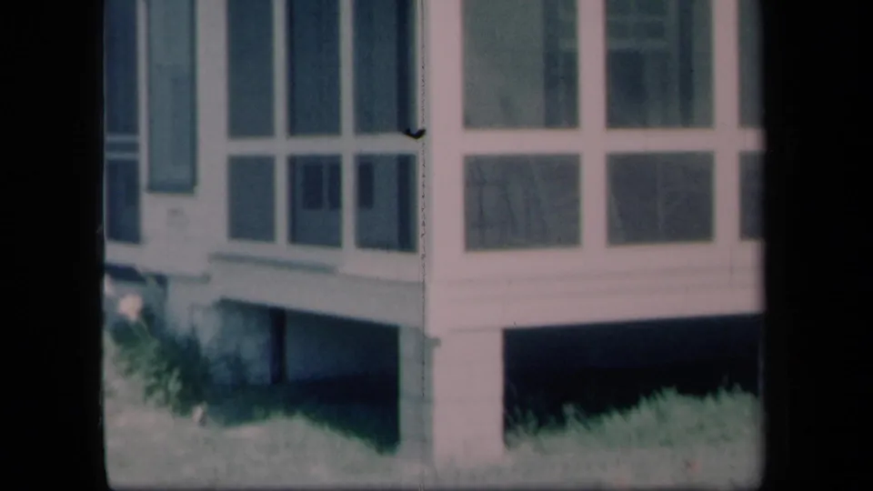 1958 New York frame showing screened porch windows, white siding, raised foundation shadow and grass beneath the house.