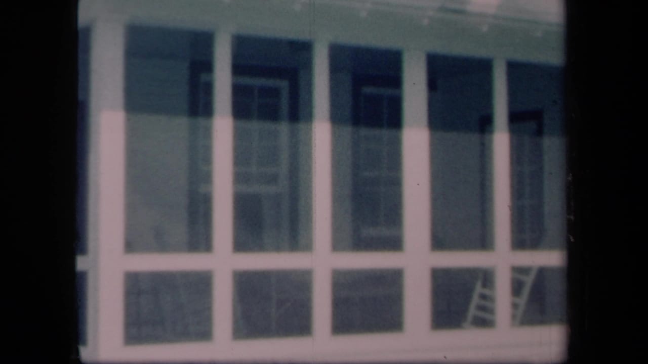 1958 New York 8mm frame showing a screened porch with tall panels, house siding, and a ladder visible through the screen.