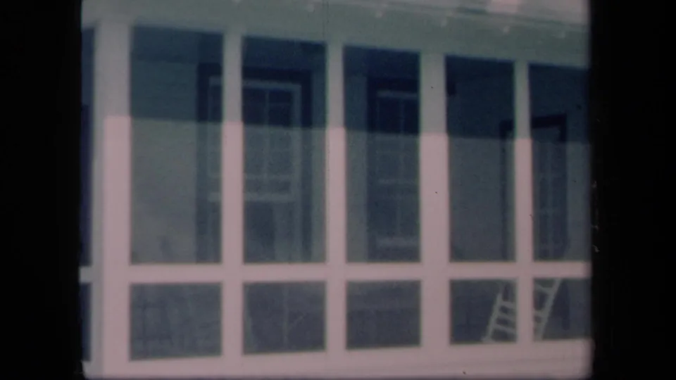 1958 New York 8mm frame showing a screened porch with tall panels, house siding, and a ladder visible through the screen.
