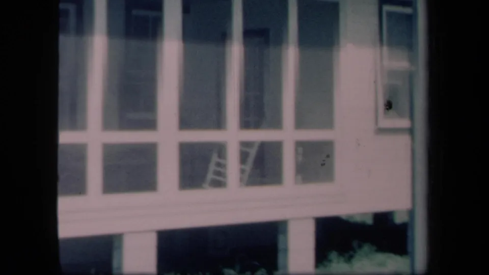 1958 New York 8mm frame showing a closer view of porch screening, siding, and an interior ladder behind the panels.