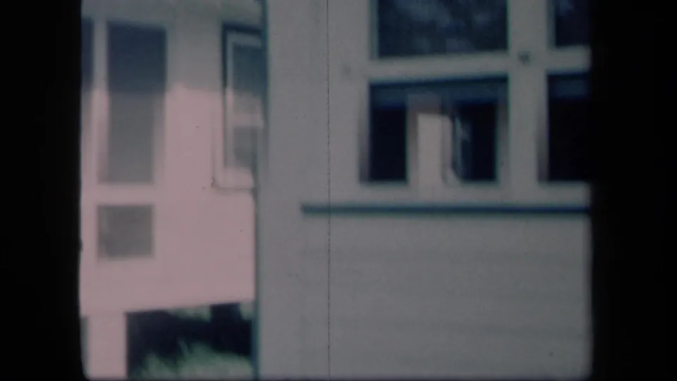 1958 New York 8mm frame showing a white residential exterior with porch structure, windows, and a dark railing or post in front.