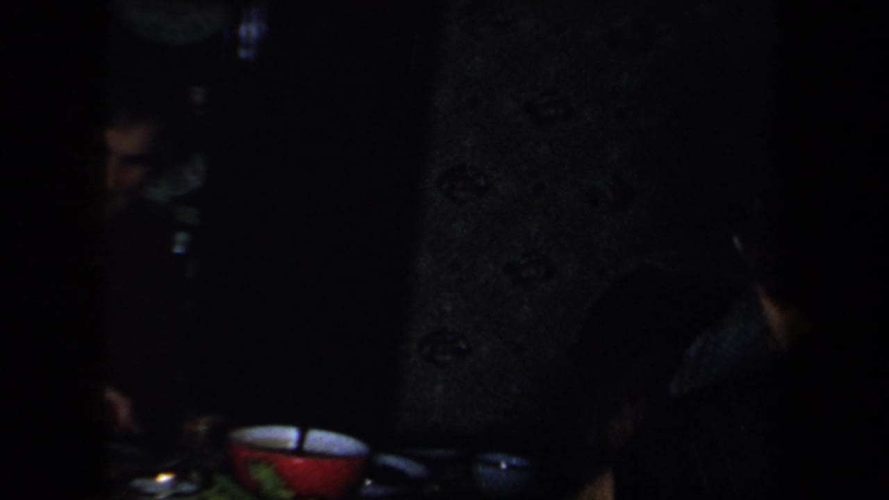 1958 New York interior frame showing adults partly obscured in shadow near a table with a red bowl, dishes, and vegetables.