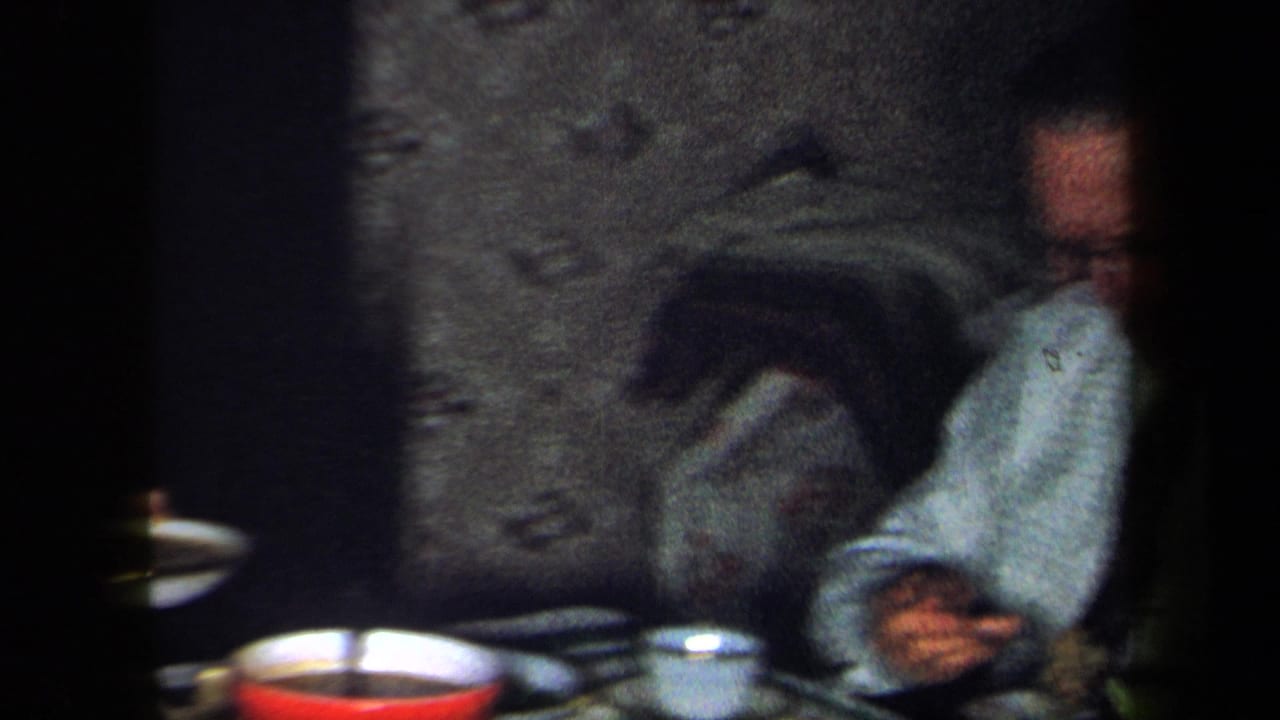 1958 New York home interior with a seated man at dinner, red bowl and tableware visible in soft 8mm focus.