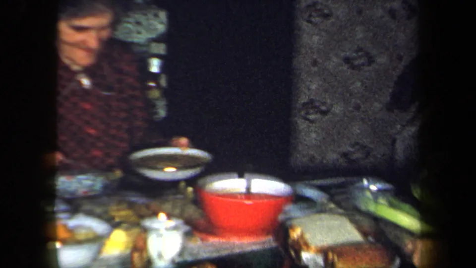 1958 New York home-movie frame showing a woman at a dinner table with plates, bowls, and serving dishes.