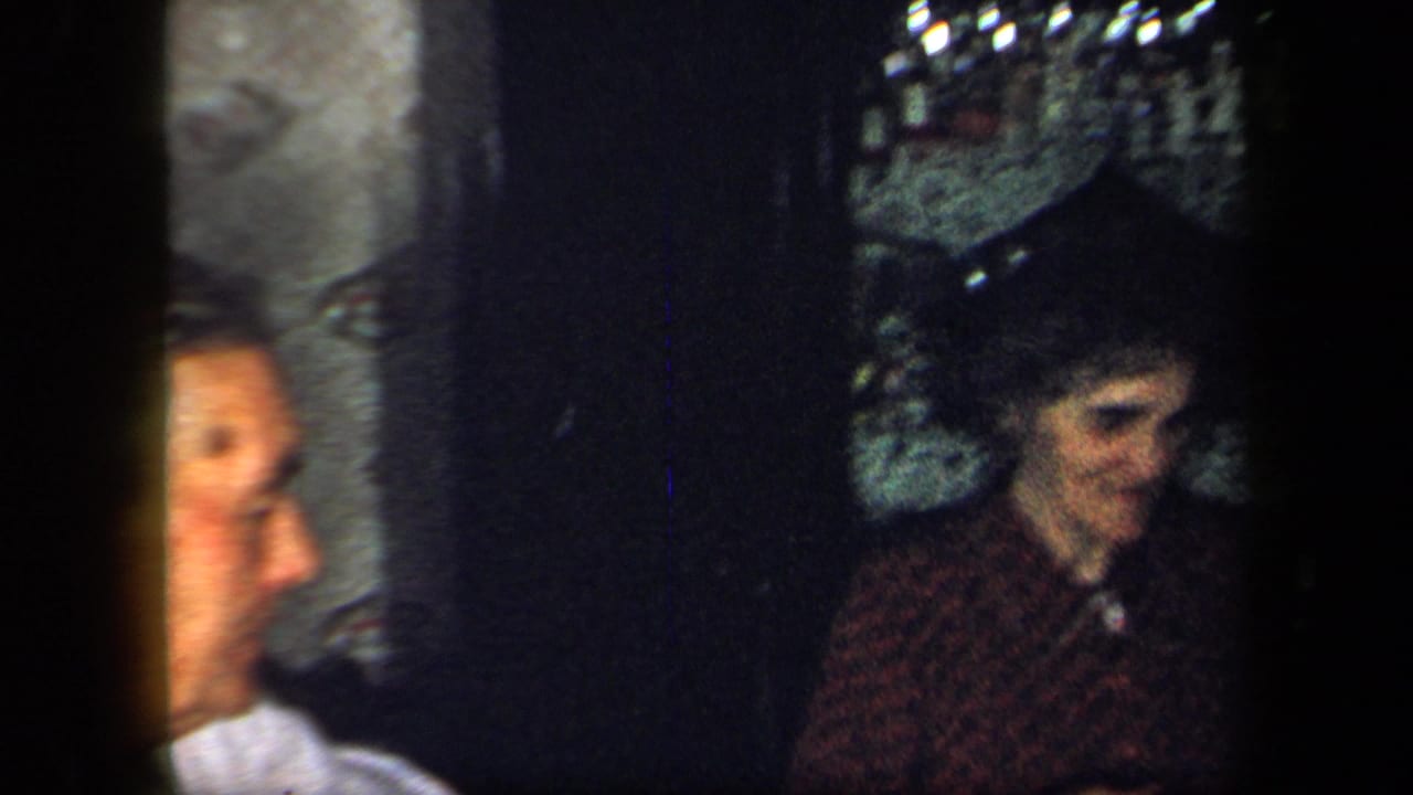 1958 New York home-movie frame showing adults seated closely in a dim interior during a family dinner.