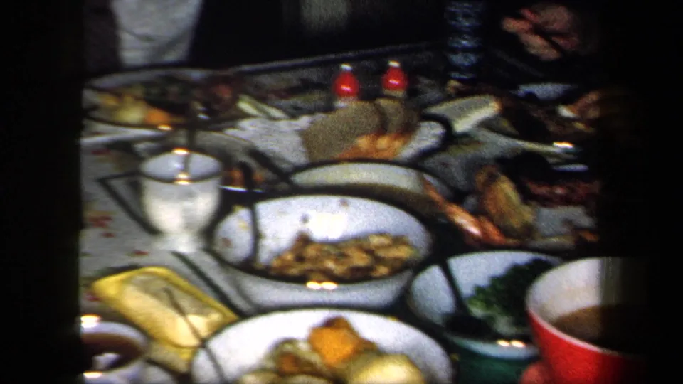 1958 New York home-movie frame focused on a family dinner table with bowls, plates, cups, bread, and assorted serving dishes.