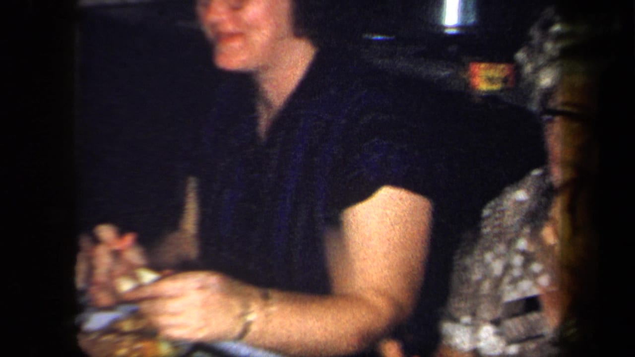 Woman in dark blouse holding food beside another seated woman with glasses.