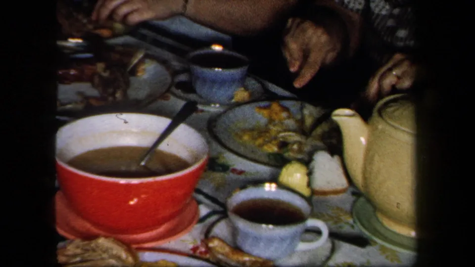 1958 New York dinner table detail with a red serving bowl, blue cups, yellow teapot, plates, and women seated at the edges.