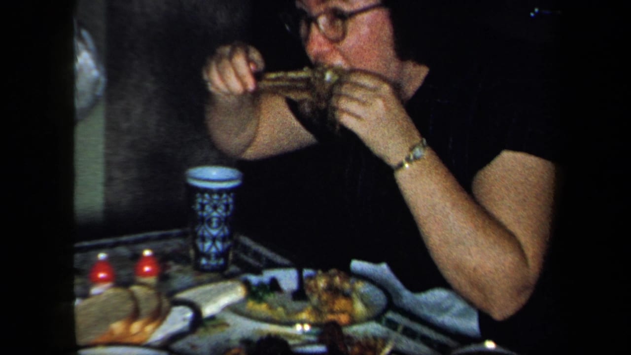 Woman with glasses eating at a dining table with plates, cups, and small red candles.