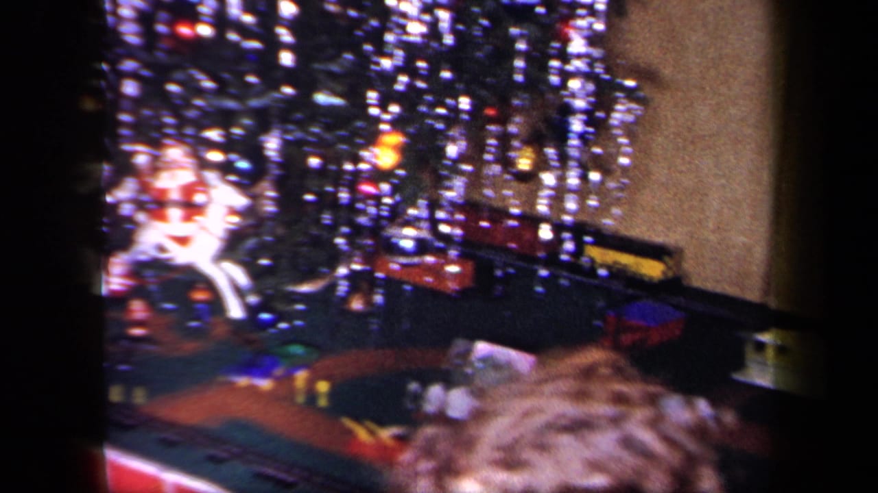 1958 New York home-movie frame showing a lit Christmas tree, toy train setup, and child seen from behind in a private interior.
