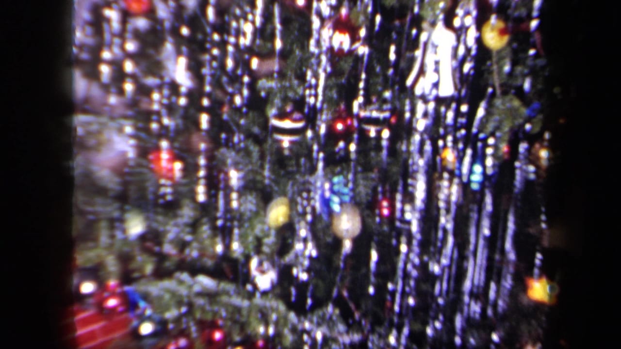 1958 New York 8mm home-movie frame showing a decorated Christmas tree with dense silver tinsel, small ornaments, and warm indoor lights.