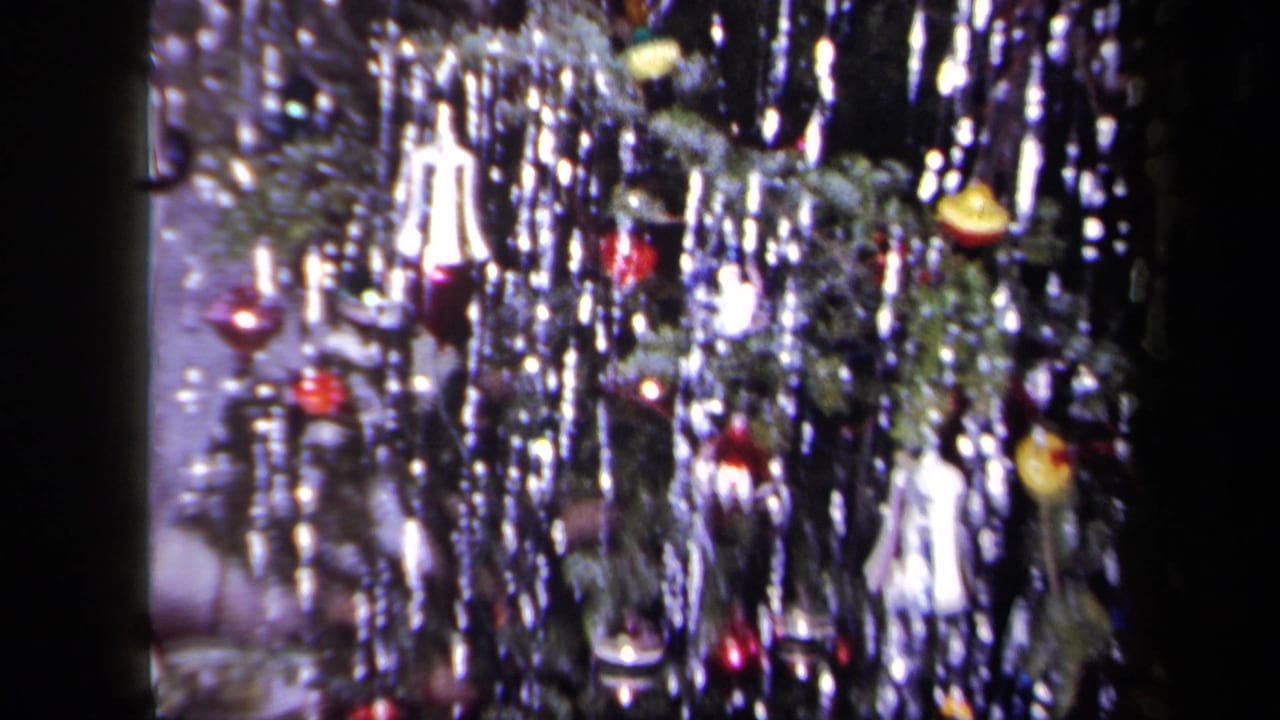Decorated Christmas tree branches with shiny tinsel, hanging ornaments, and blurred lights.