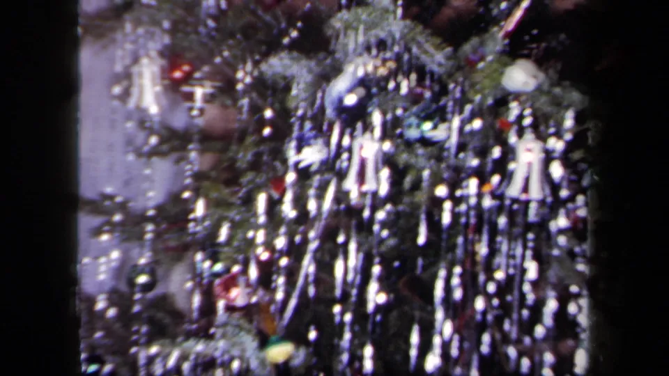 1958 New York home-movie frame capturing the tree's tinsel, hanging baubles, and reflective holiday lights in soft 8mm color.