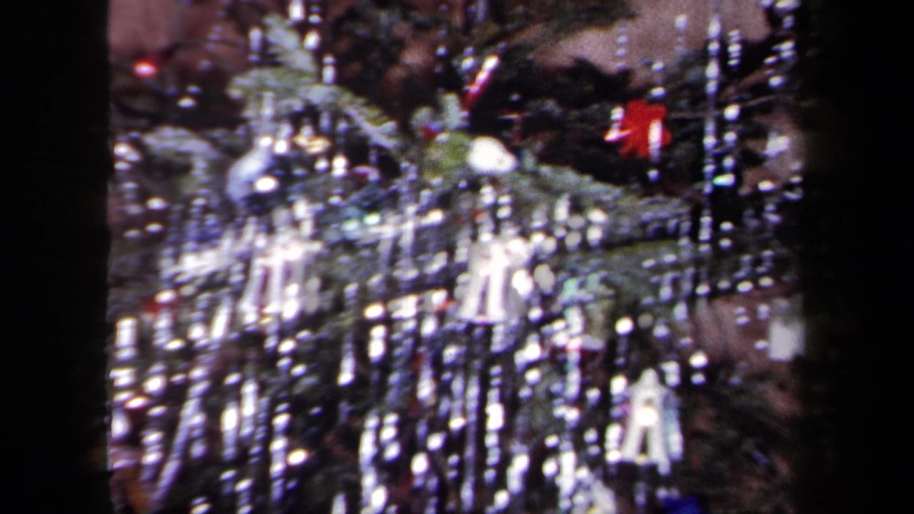 1958 New York home-movie frame showing a Christmas tree with dense silver tinsel, baubles, and small hanging decorations.