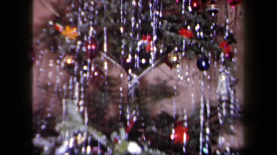 1958 New York 8mm frame of decorated Christmas tree branches with silver tinsel, colorful baubles, and small angel-like ornaments.