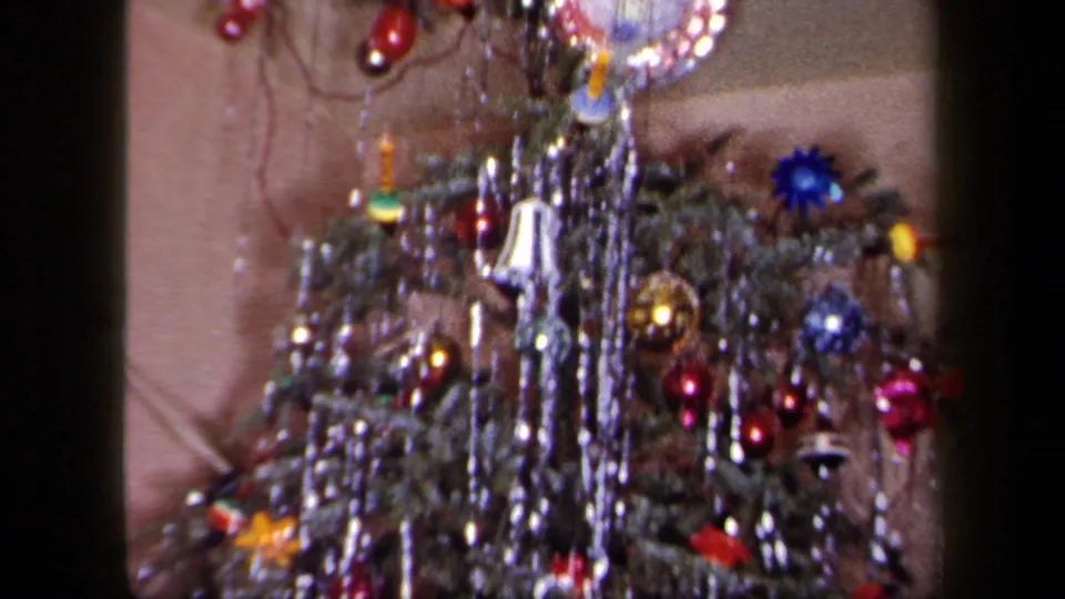 1958 New York home-movie still of lower Christmas tree branches with blue and red ornaments, silver tinsel, and small decorations.