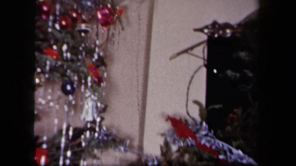 1958 New York 8mm frame showing the decorated Christmas tree beside a dark household object, with tinsel and ornaments visible.