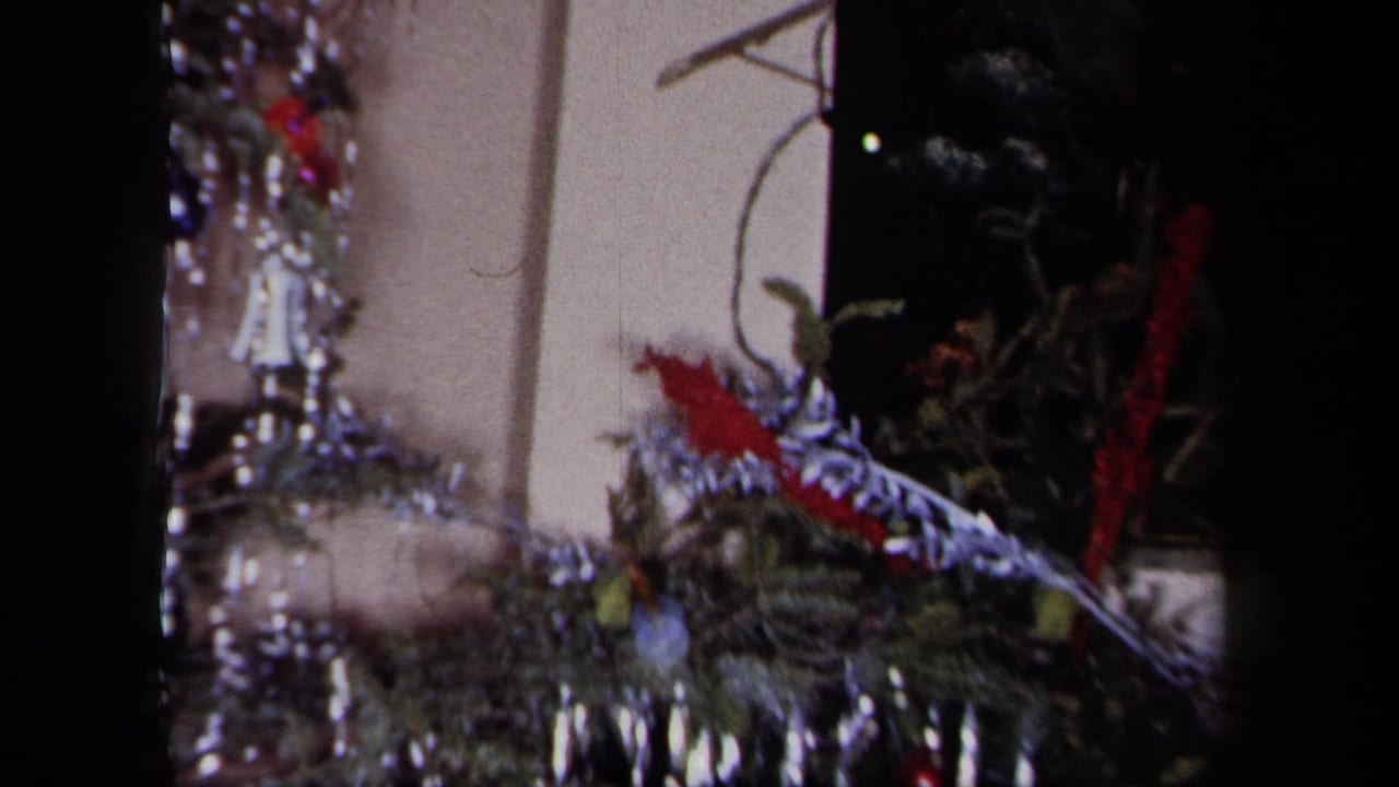 1958 New York home-movie frame showing evergreen decor, tinsel and red holiday accents on a mantel.