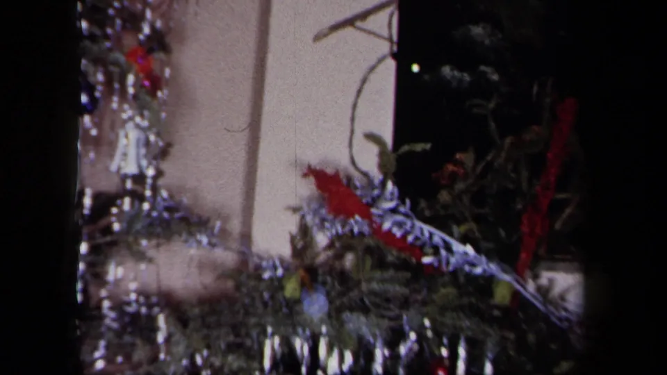1958 New York home-movie frame showing evergreen decor, tinsel and red holiday accents on a mantel.