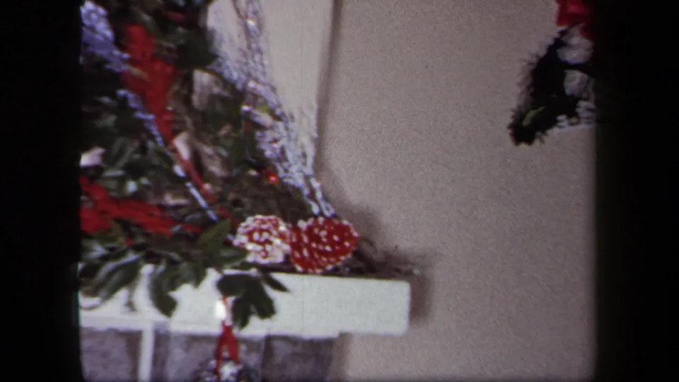 1958 New York frame showing a side detail of Christmas mantel greenery, silver tinsel, red pinecones and ornaments.