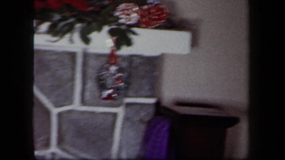 1958 New York home-movie frame showing a stone fireplace area with Christmas decorations and a red stocking.