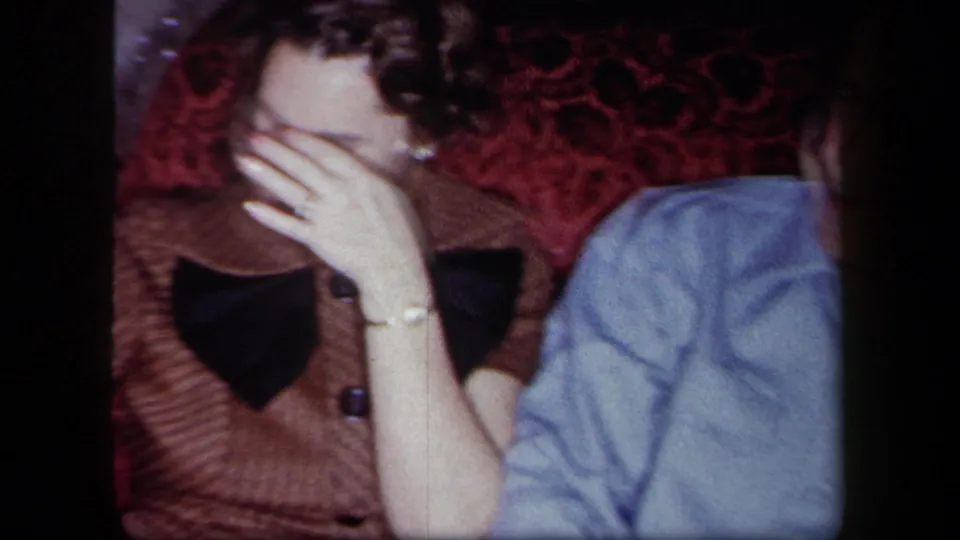 1958 New York home-movie frame showing a seated woman laughing and covering her face during a holiday gathering.