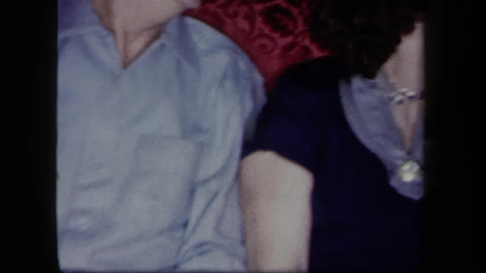 1958 New York home-movie frame with seated adults cropped close, including a woman in blue with pearls.