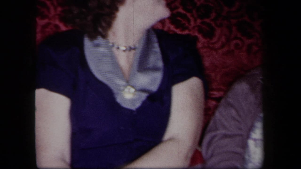 Younger woman in a dark dress sits beside another adult in a softly lit interior.