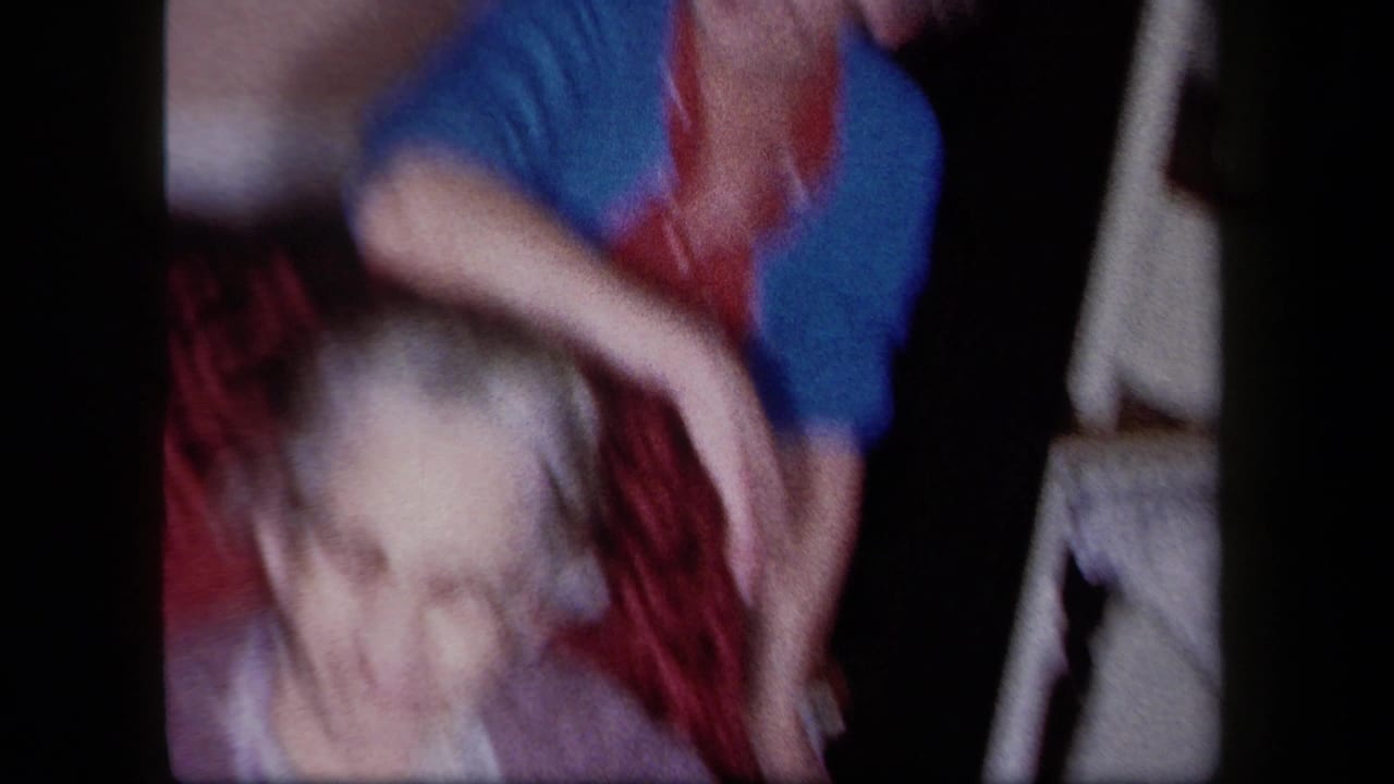 1958 New York 8mm frame showing an older woman with glasses and another adult close behind her in a private interior.