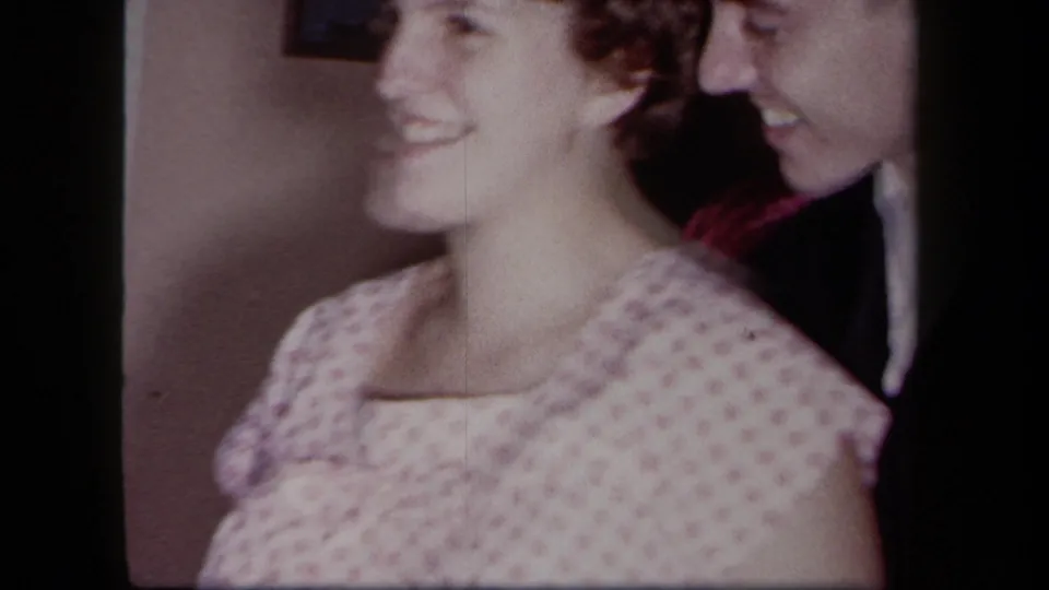 1958 New York 8mm home-movie frame of a smiling younger couple seated closely together indoors.