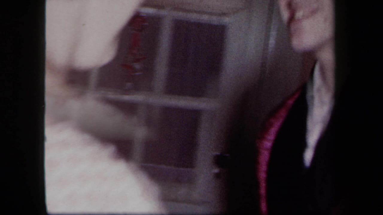 1958 New York home-movie frame showing two adults in close dance posture near a window, with faces partly cropped and soft exposure.