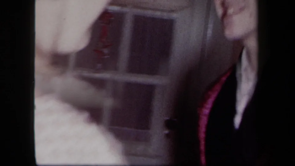 1958 New York home-movie frame showing two adults in close dance posture near a window, with faces partly cropped and soft exposure.