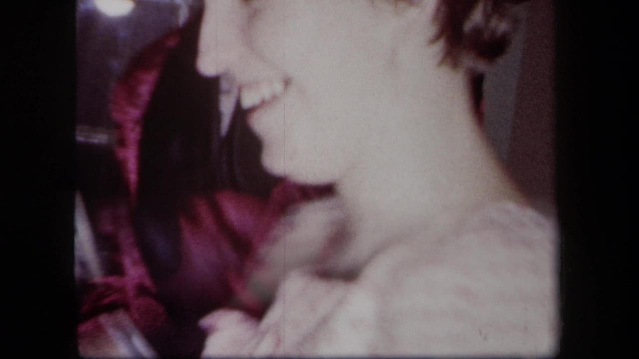 Smiling woman in a light dress faces a man in a maroon robe indoors.