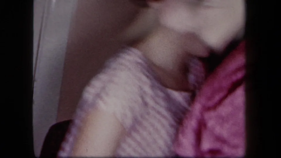 1958 New York home-movie frame showing a smiling woman in a patterned dress beside a man in maroon clothing during an indoor dance.