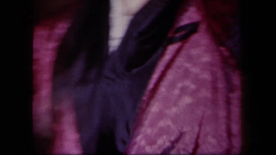 Close handheld 8mm frame of party movement, with pink fabric and a dark jacket filling most of the New York interior scene.
