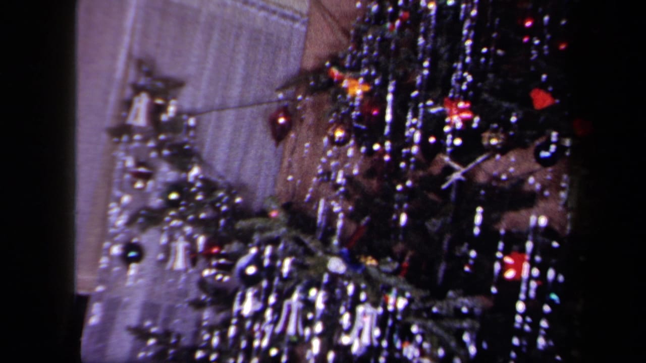 Close interior view of a decorated Christmas tree in 1958 New York footage, with shiny tinsel, baubles and bell-shaped ornaments.