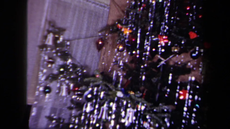 Close interior view of a decorated Christmas tree in 1958 New York footage, with shiny tinsel, baubles and bell-shaped ornaments.