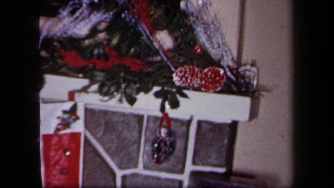 1958 New York Christmas interior with a garlanded stone fireplace and red stocking hanging near the mantel.