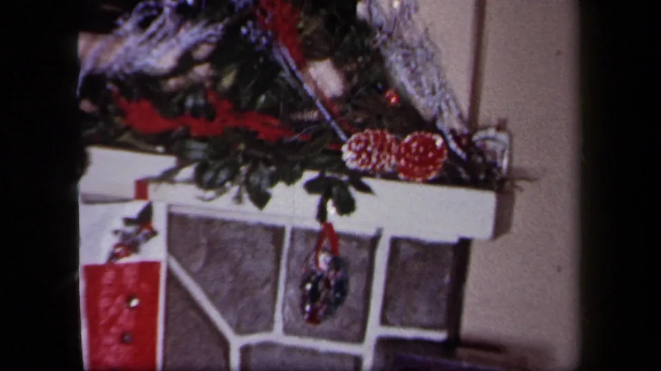 1958 New York Christmas interior with a garlanded stone fireplace and red stocking hanging near the mantel.