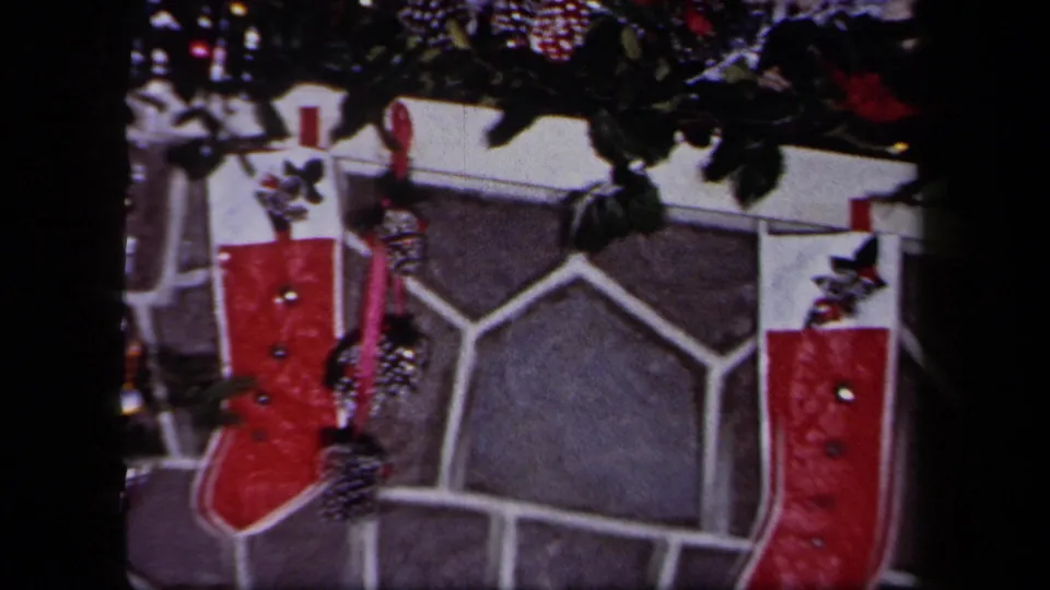 1958 8mm frame of a New York home fireplace, showing stonework, mantel garland, ribbon, and a red Christmas stocking.